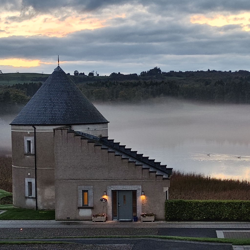 mist on a lake behind a stone building with a round tower shaped slate roof